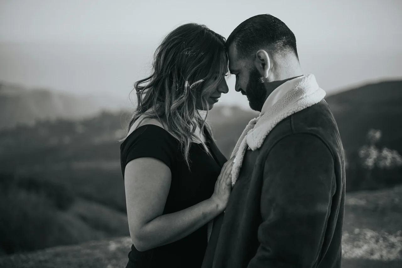 A couple standing forehead to forehead in open country.